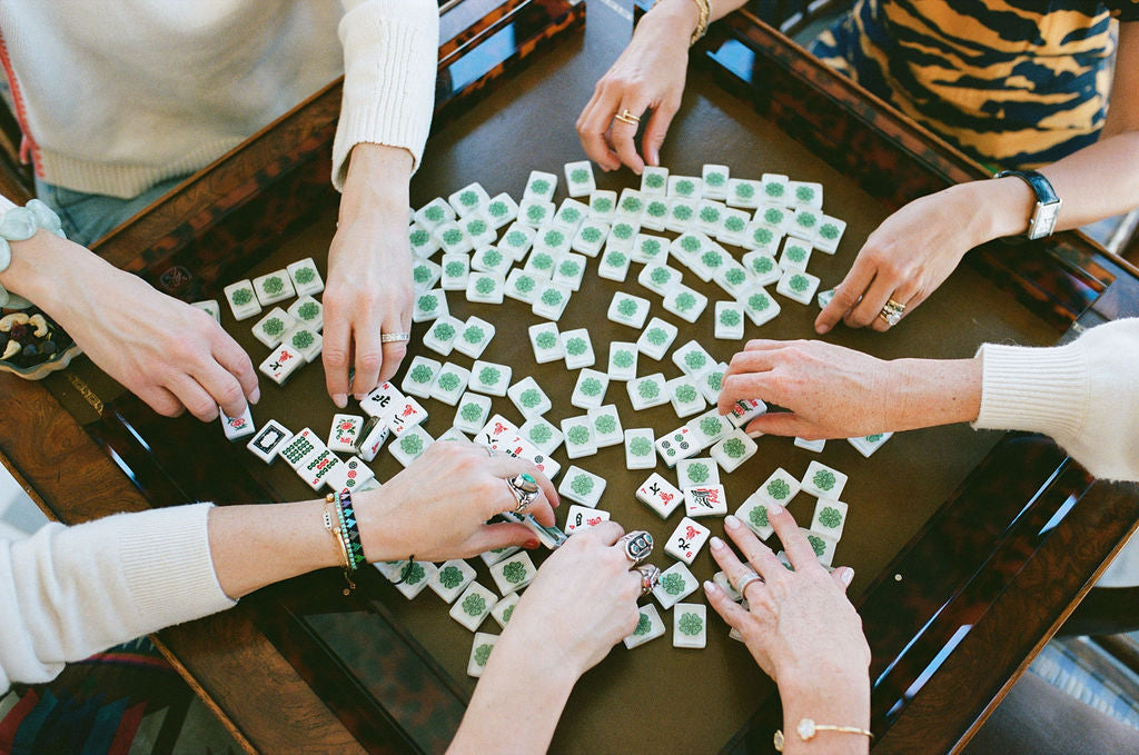 People playing a game of mahjong  with green and white tiles on a wooden table.  | The Pepper Pot Barrington, IL 