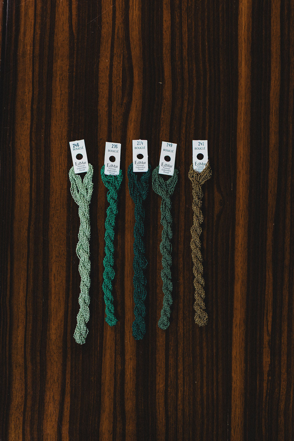 Five green yarn thread samples on a wooden surface from Boucle.  | The Pepper Pot Barrington, IL 