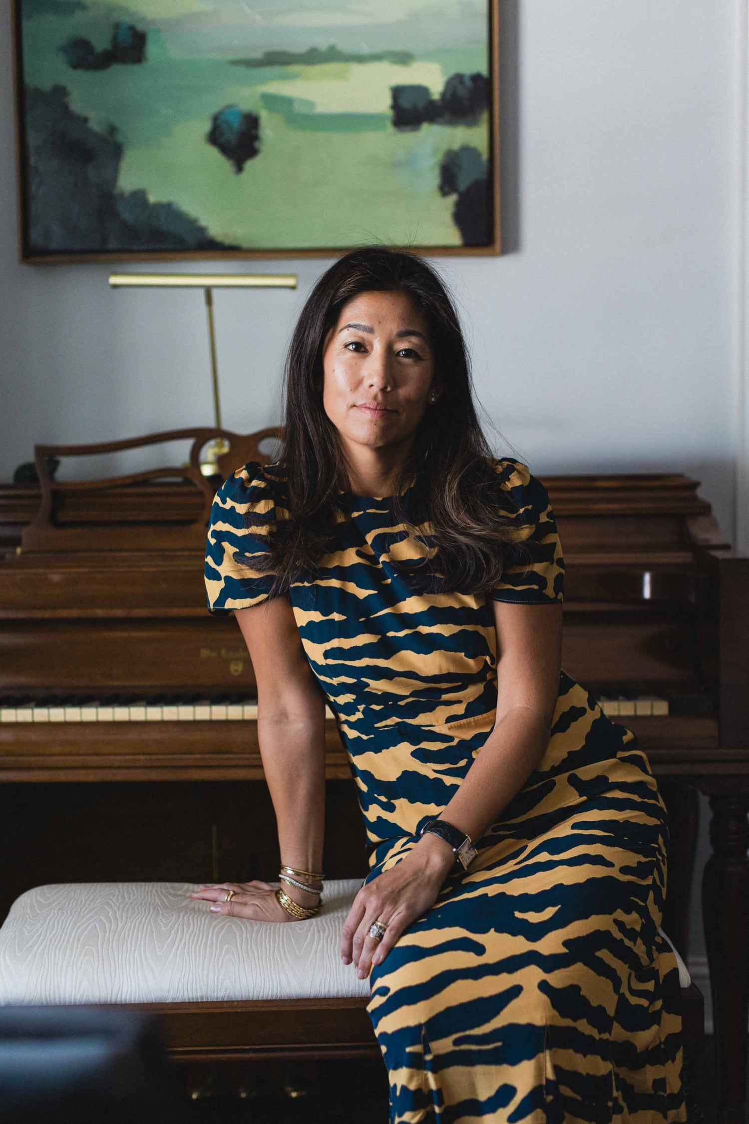 Crystal Pepper, Owner of The Pepper Pot in Barrington, IL. Wearing a tiger-striped dress sitting in front of a piano with a painting on the wall.