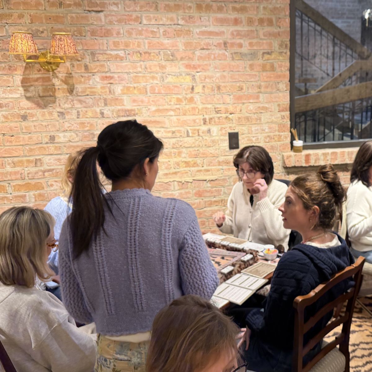 Group of people sitting around a table in a casual setting playing American Mahjong with a brick wall background at The Pepper Pot in Barrington, IL