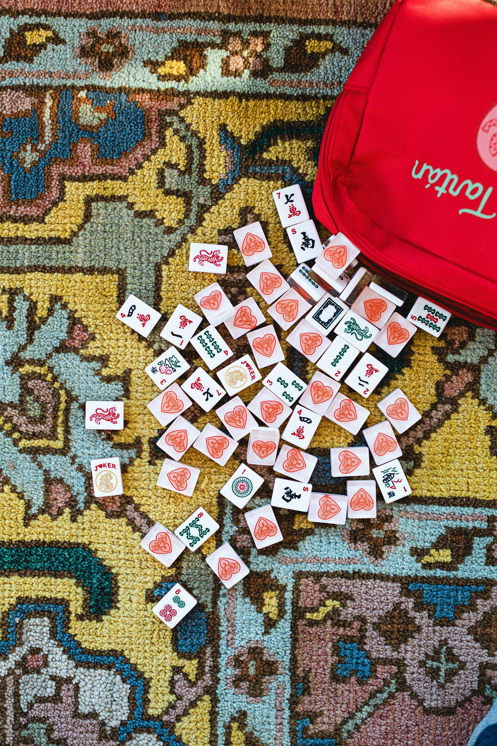 Mahjong tiles on a patterned rug with a red bag labeled 'Tartan' in the background.  | The Pepper Pot Barrington, IL 