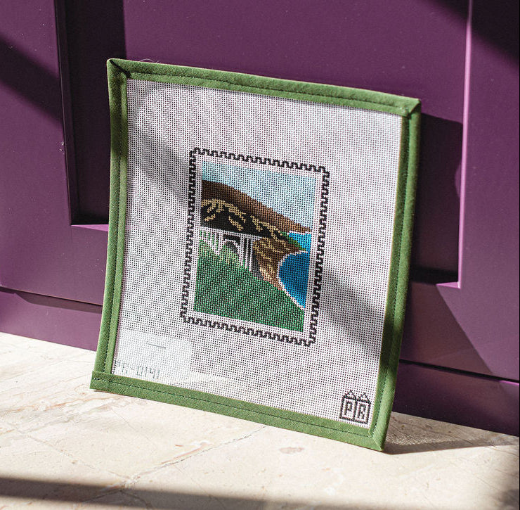 Framed needlepoint canvas on a purple surface with a white mat. The Pepper Pot in Barrington, IL