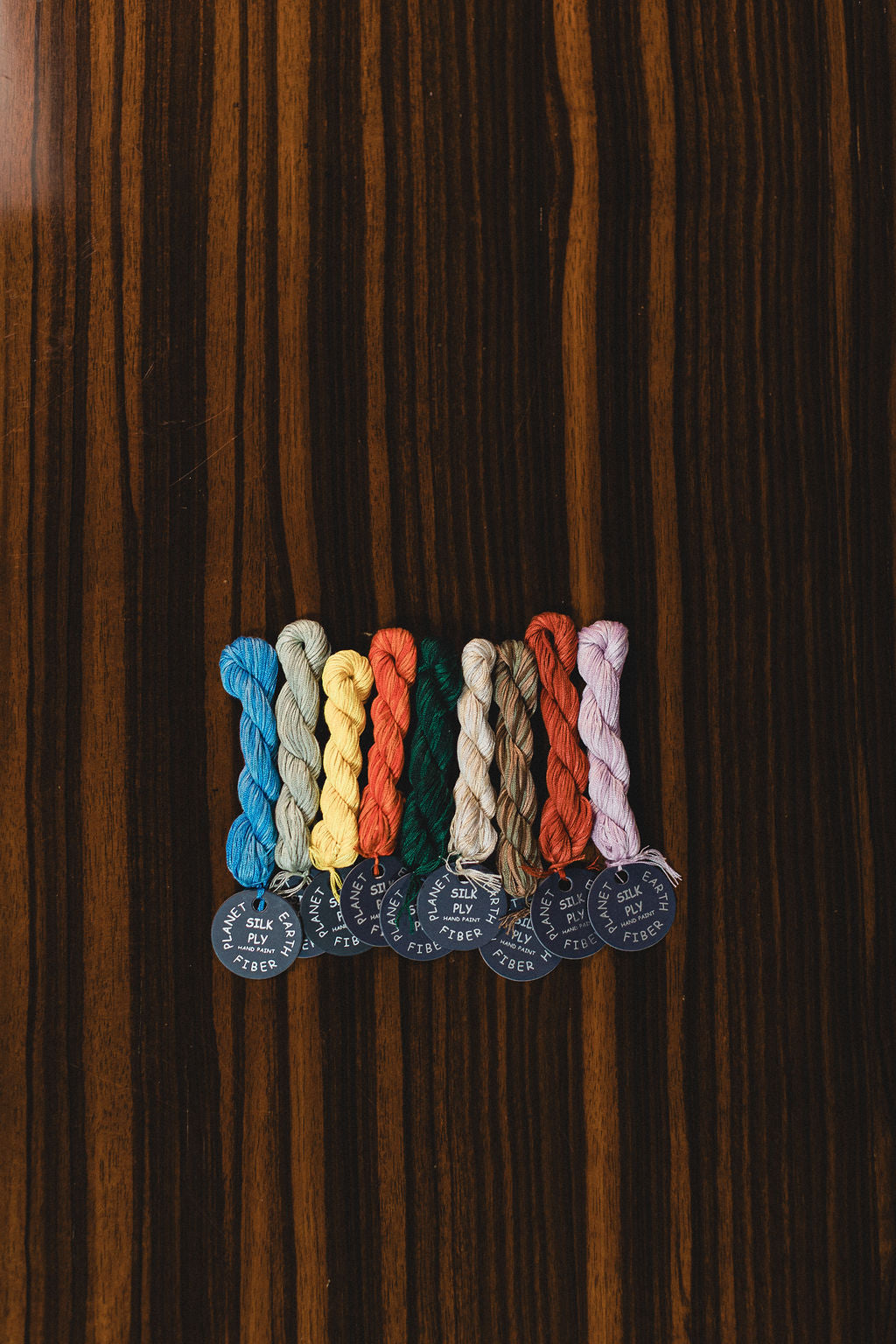Set of colorful braided silk ply threads on a wooden surface from Planet Earth Fiber company.  | The Pepper Pot Barrington, IL 