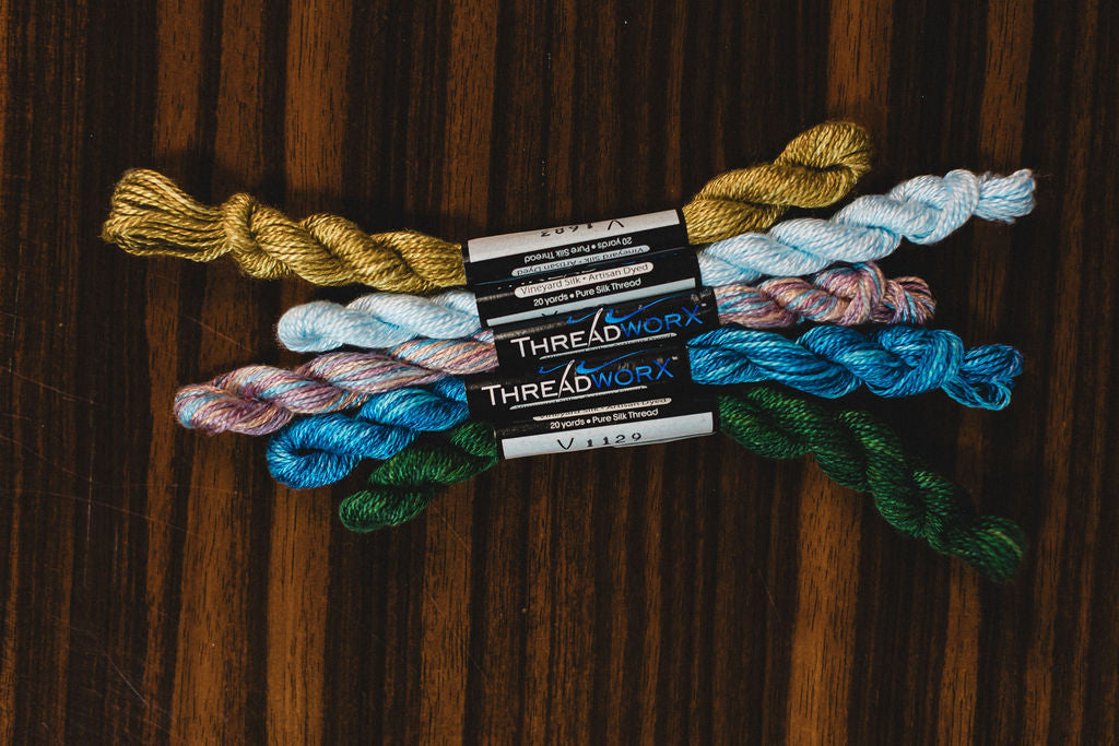 Colorful yarn skeins and ThreadWorx packaging on a wooden surface.  | The Pepper Pot Barrington, IL 