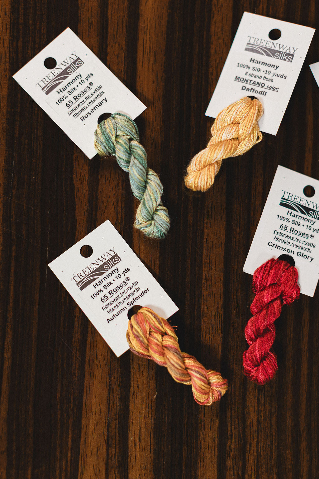 Four skeins of thread in different colors with labels on a wooden surface from Treenway Silks.  | The Pepper Pot Barrington, IL 