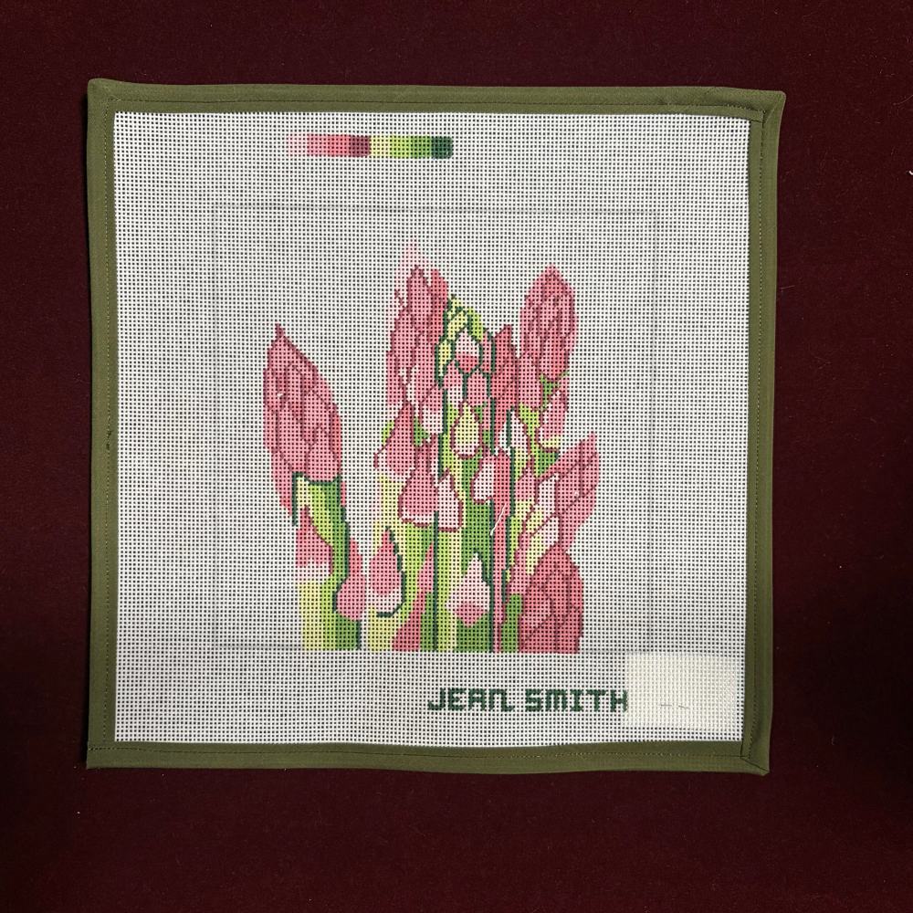Needlepoint canvas design of pink asparagus flowers on a white fabric with green border, signed 'Jean Smith'.