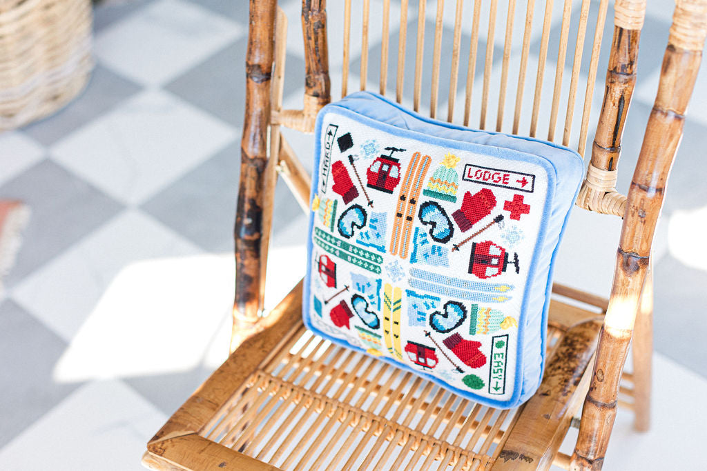 Decorative needlepoint pillow with ski and alpine  themed design on a wicker chair. | The Pepper Pot, Barrington, IL