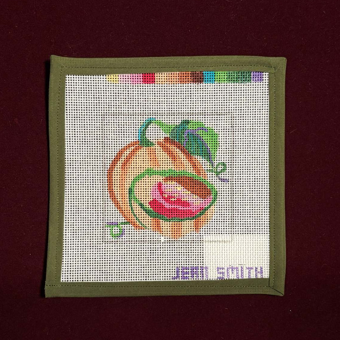 Needlepoint canvas with a colorful cantaloupe design on a white background, framed by a green border.