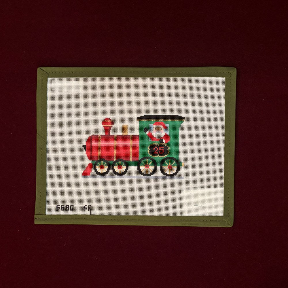 Needlepoint canvas design of a red and green train with Santa on a beige background, framed by a green border.