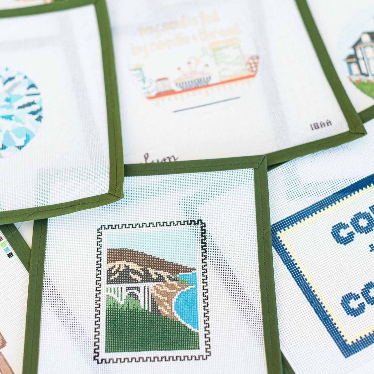 Collection of needlepoint canvases available at The Pepper Pot in Barrington, IL on fabric with green frames.