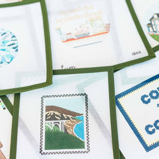 Collection of needlepoint canvases available at The Pepper Pot in Barrington, IL on fabric with green frames.