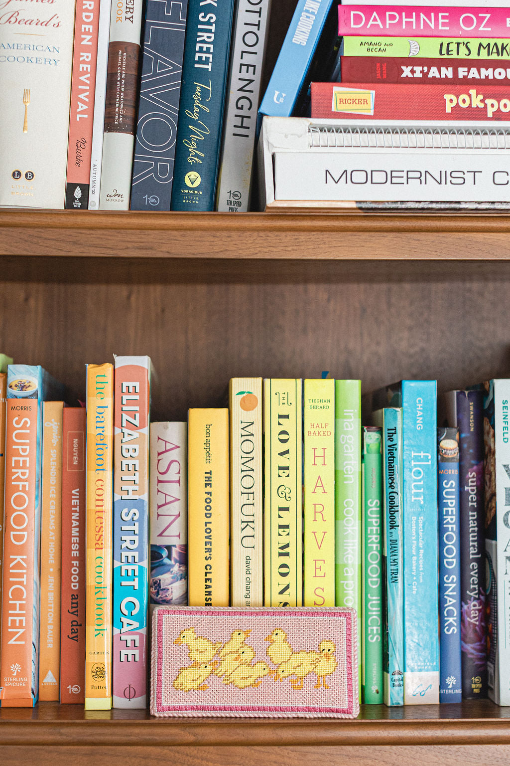 Wooden shelf with books and a pink needlepoint bookend with gold chicks on a wooden surface.  | The Pepper Pot Barrington, IL 