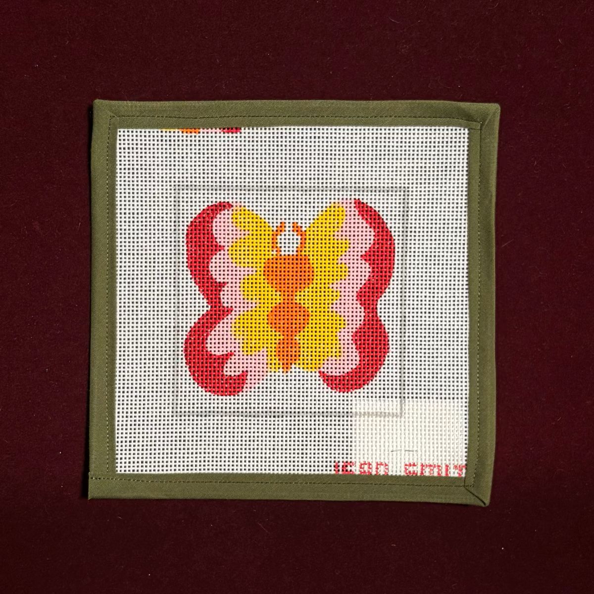 Butterfly design on a needlepoint canvas with a red border on a dark red background