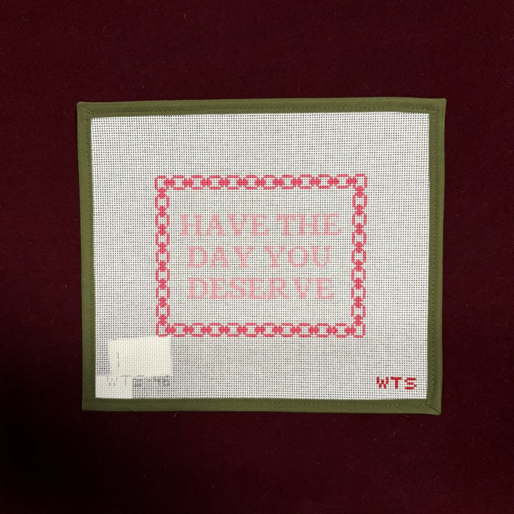 Needlepoint canvas design with 'Have the day you deserve' text on a white fabric background, framed by a green border.