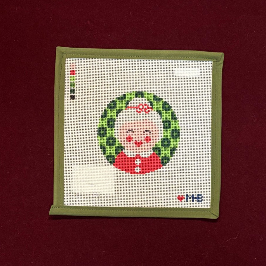 Needlepoint canvas design of a Mrs. Claus face with a wreath on a red background
