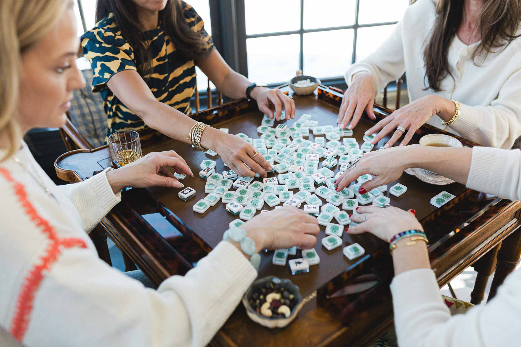 People playing a mahjong game with tiles on a wooden table. The Pepper Pot | Needlepoint and Mahjong Specialty Store in Barrington, IL