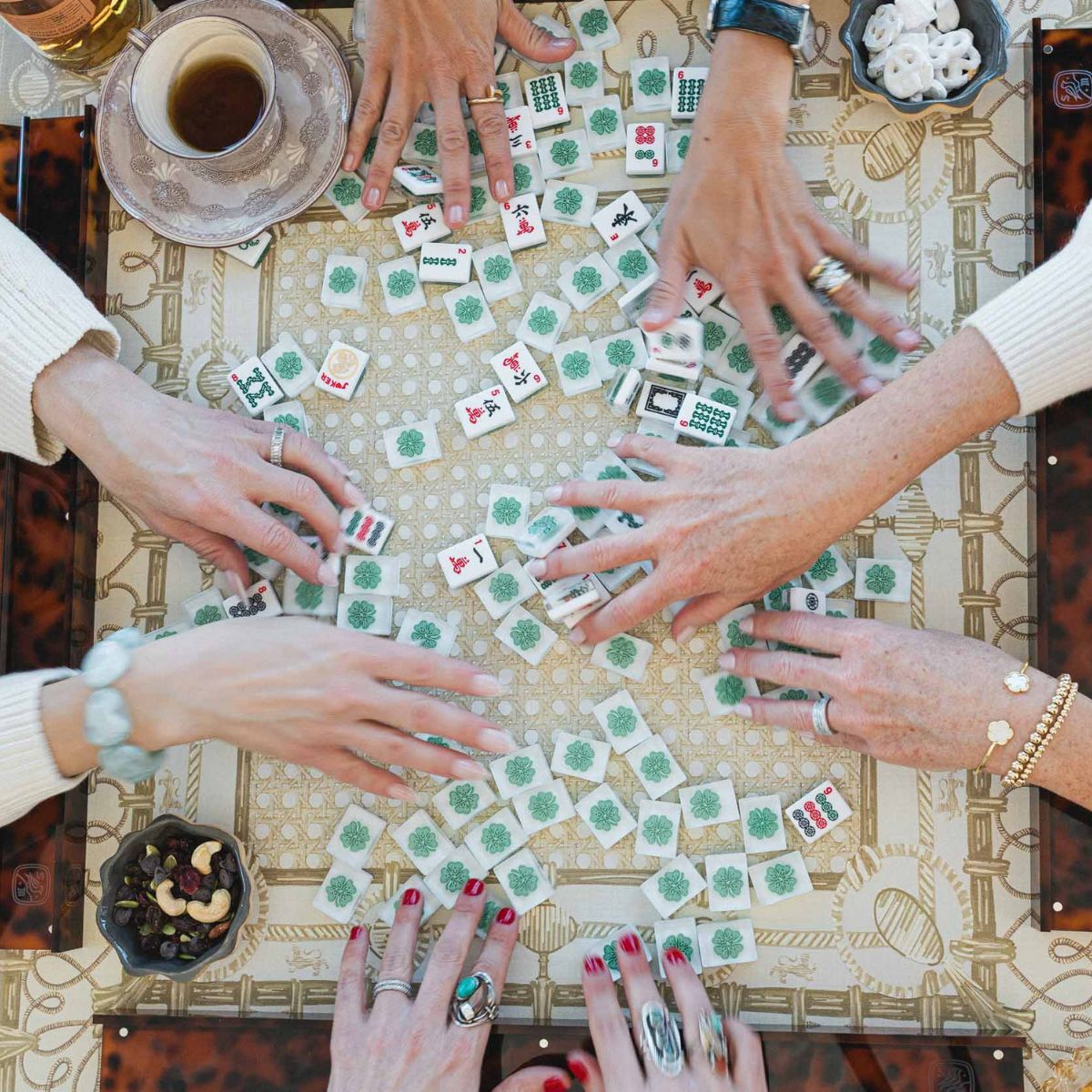 Group of people playing a game  of American Mahjong with mahjong tiles on a patterned mahjong mat.