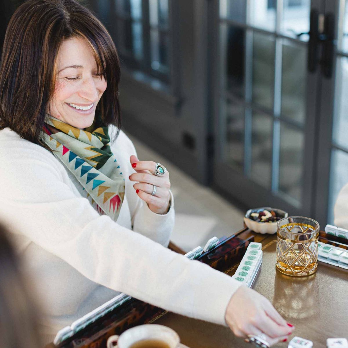 Woman playing a mahjong  game at a table with a colorful scarf and a glass of water at The Pepper Pot in Barrington, IL. 