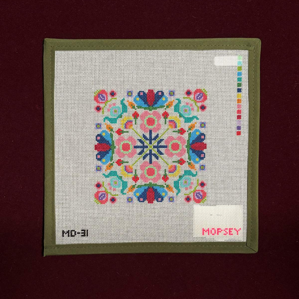 Colorful needlepoint canvas  on a fabric panel with 'Mopsey' branding on a dark red background