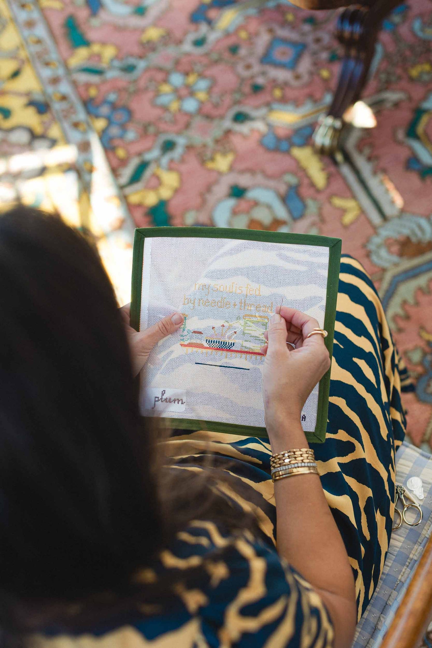 Person holding a needlepoint canvas with a colorful patterned rug in the background. The Pepper Pot | Needlepoint and Mahjong Specialty Store in Barrington, IL