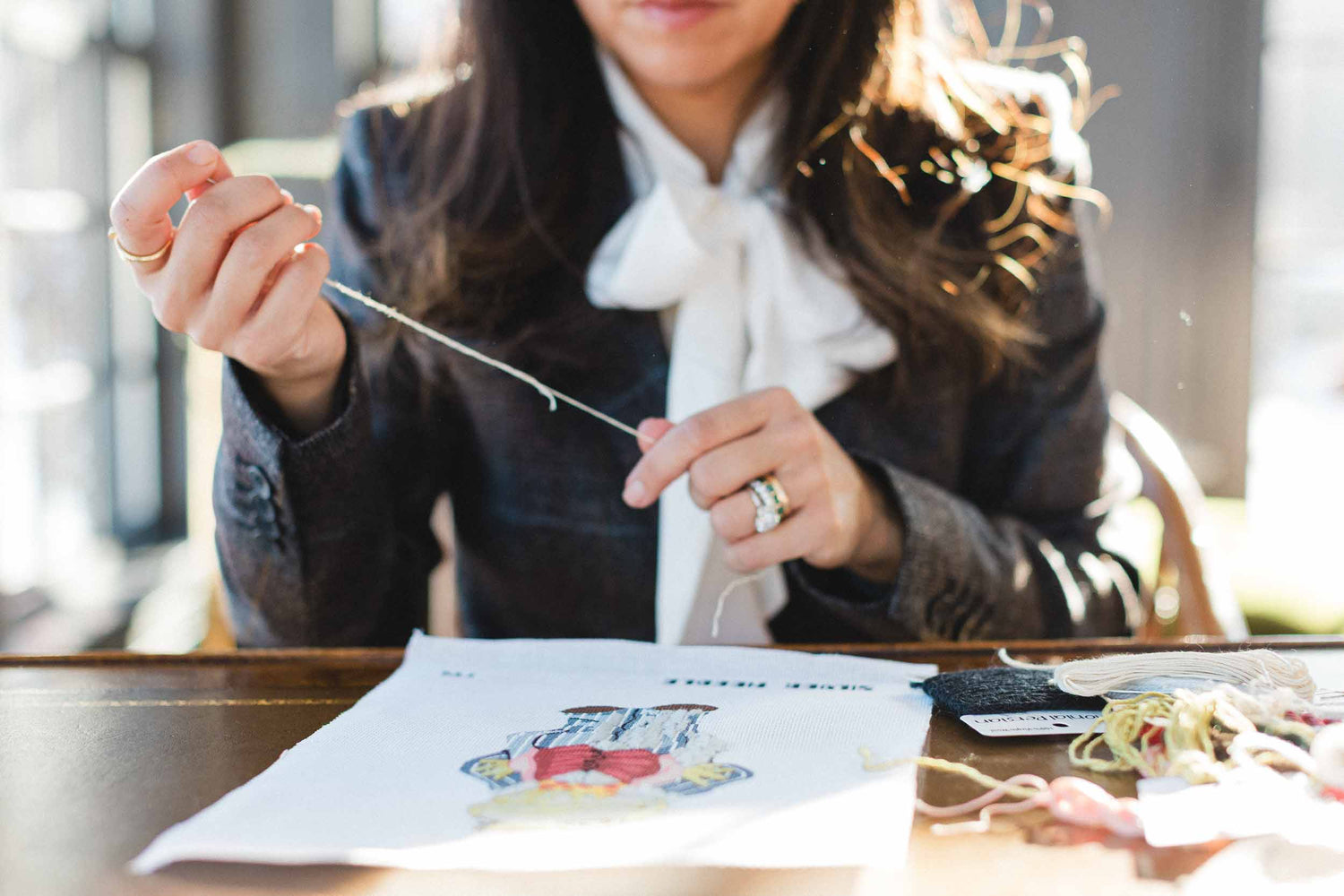 Person sitting at a table with a cross-stitching project and materials. | The Pepper Pot, Barrington, IL