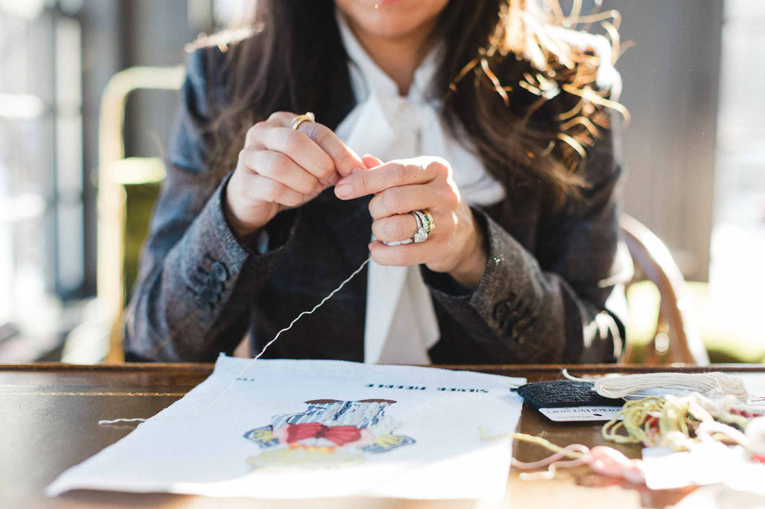 Person engaged in cross-stitching and needlepoint at a table with a blurred background. | The Pepper Pot Barrington, IL 