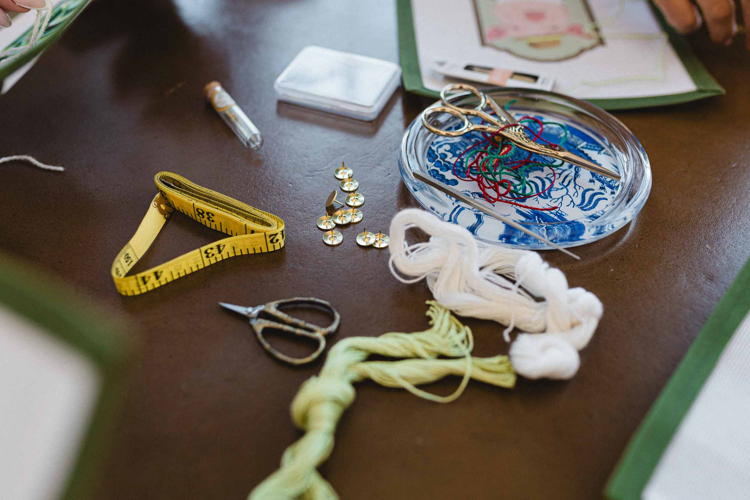 Crafting materials including a tape measure, scissors, buttons, and yarn on a wooden surface. | The Pepper Pot, Barrington, IL