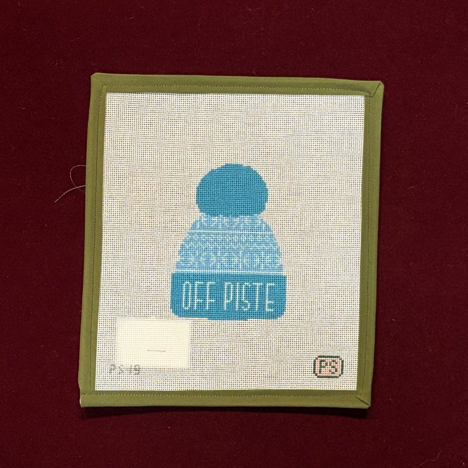 Needlepoint canvas with blue knit cap design and 'OFF PISTE' text on a red background