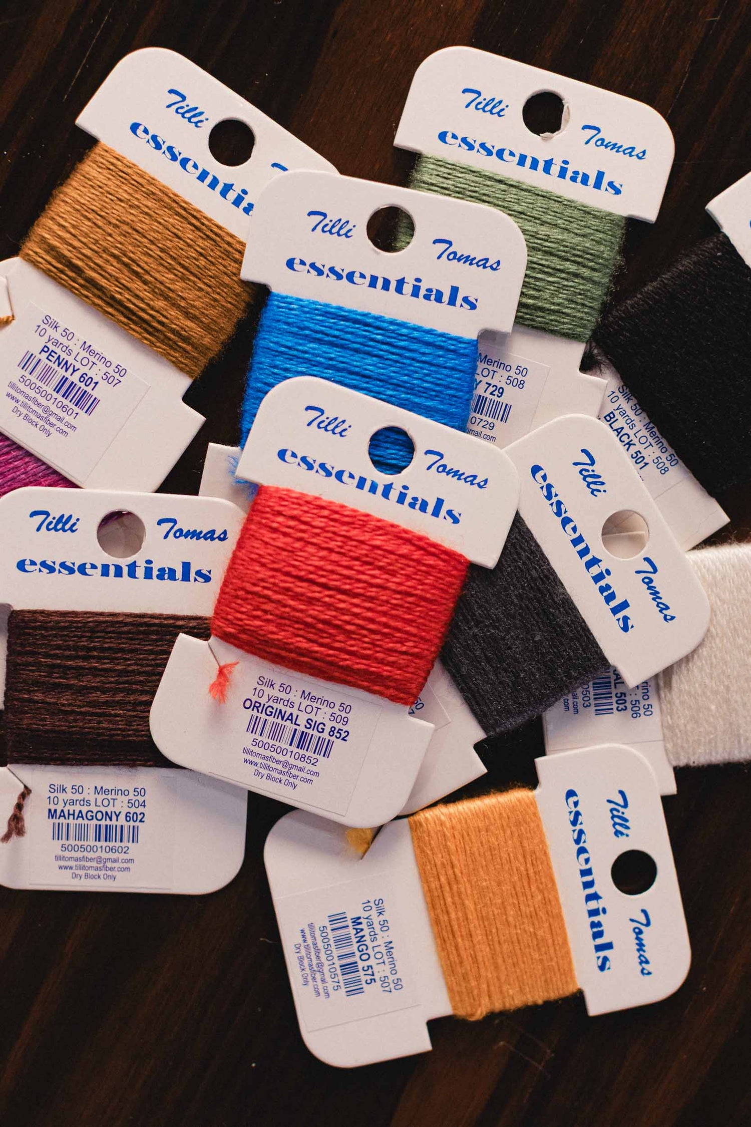 Assorted cards of needlepoint  thread with 'Tilli Tomas essentials' labels on a dark surface. | The Pepper Pot, Barrington, IL