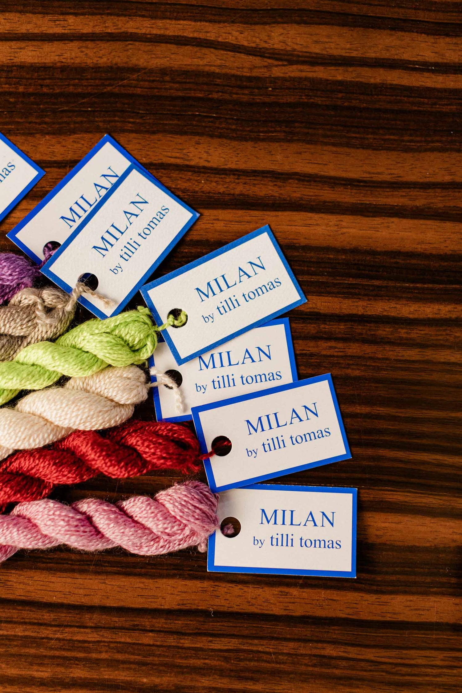 Needlepoint Yarn skeins with 'Milan by tilli tomas' labels on a wooden surface. | The Pepper Pot, Barrington, IL