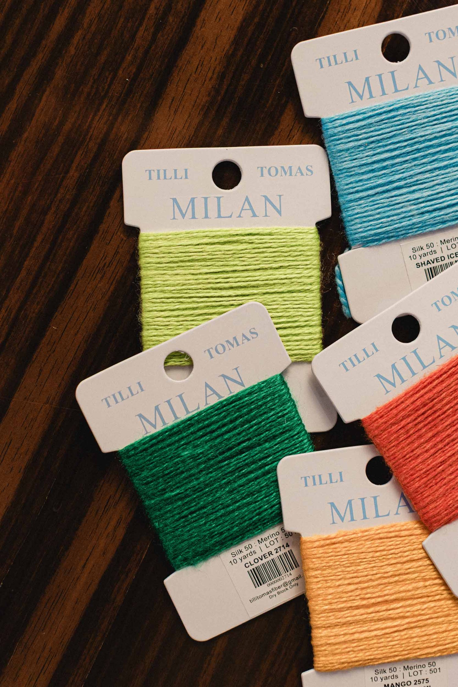 Color swatches of yarn on brand Tilly & Tomas Milan cards against a wooden background. | The Pepper Pot, Barrington, IL