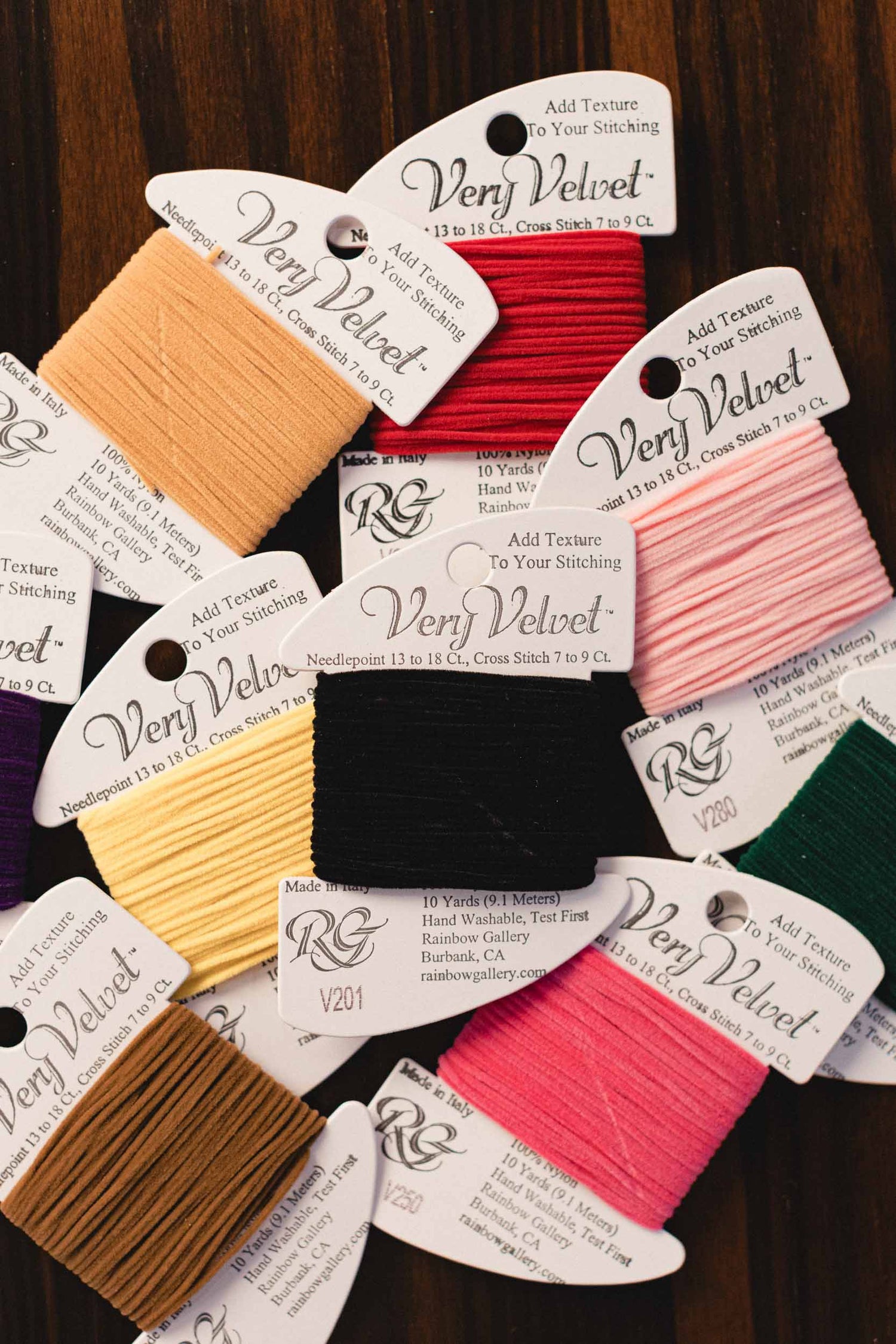 Collection of Very Velvet thread spools with colorful labels on a wooden surface.  | The Pepper Pot Barrington, IL 