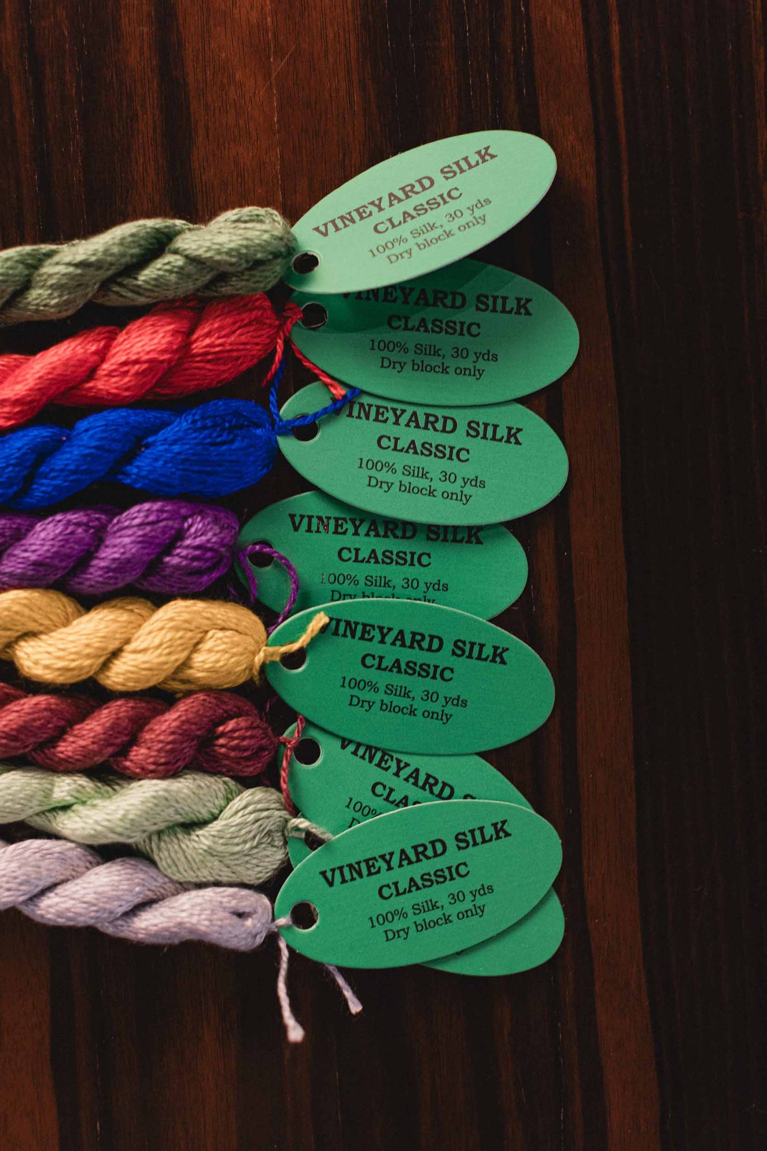 Vineyard Silk Classic. 100% Silk. 30 yards. Dry block only.  Colorful yarn skeins with green tags on a wooden background. | The Pepper Pot, Barrington, IL