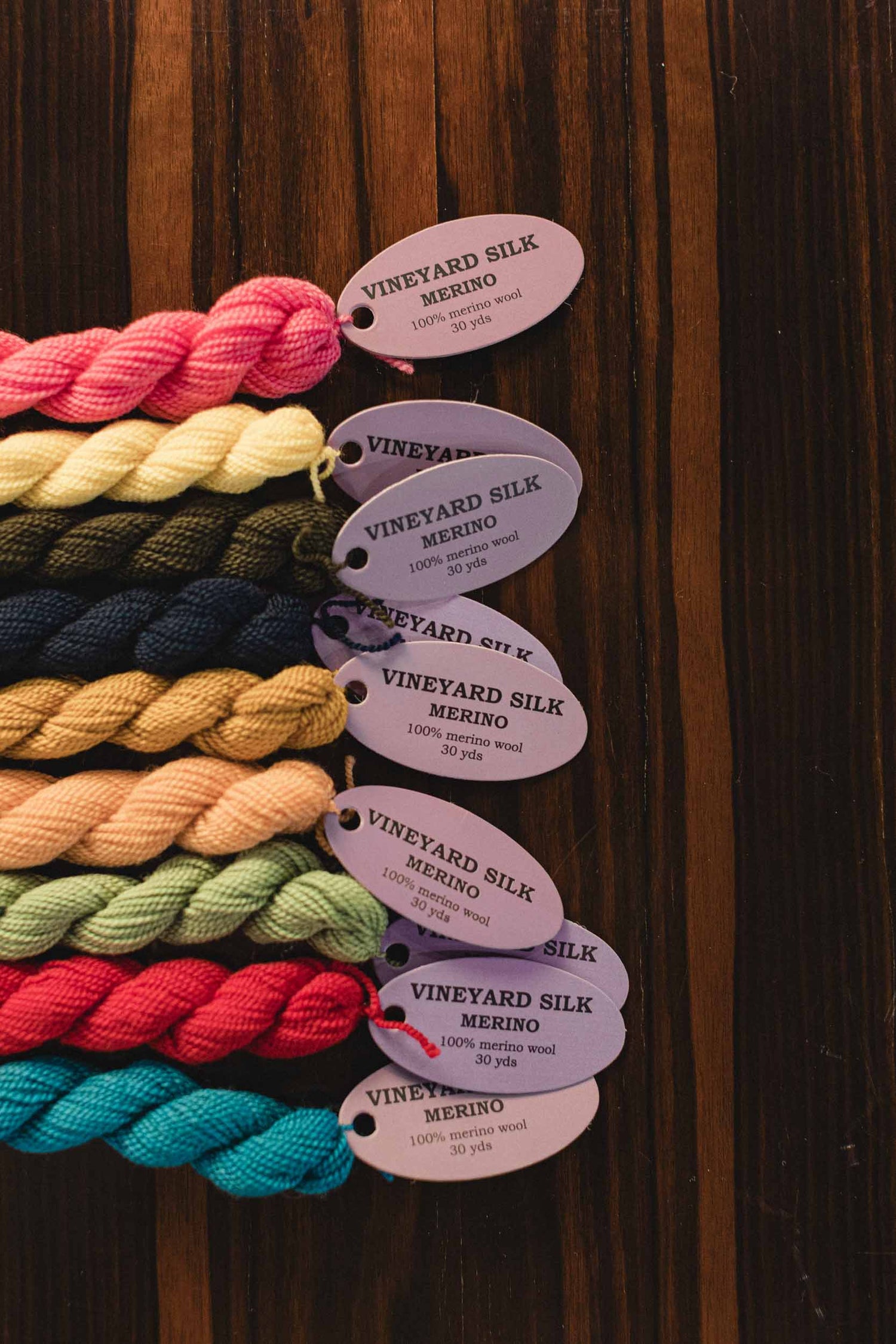 Vineyard Silk Merino. 100% merino wool. 30 yards. Color swatches of yarn with labels on a wooden board. | The Pepper Pot, Barrington, IL