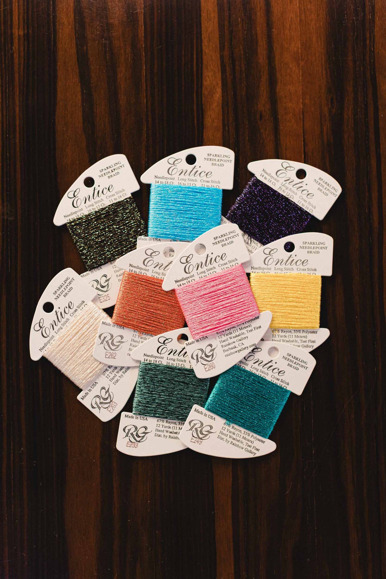 Assorted spools of embroidery threads from brand Entice on display against a dark background. | The Pepper Pot, Barrington, IL