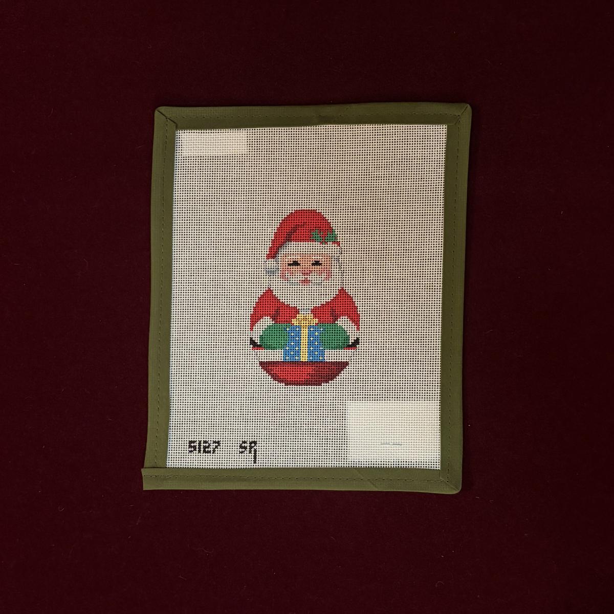 Needlepoint picture of Santa Claus holding a gift on a dark red background