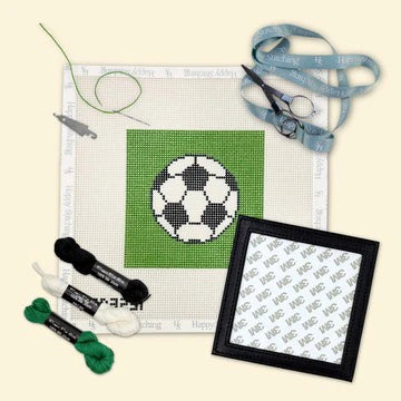 Cross-stitching kit with a soccer ball design on fabric, thread, scissors, and a hoop.