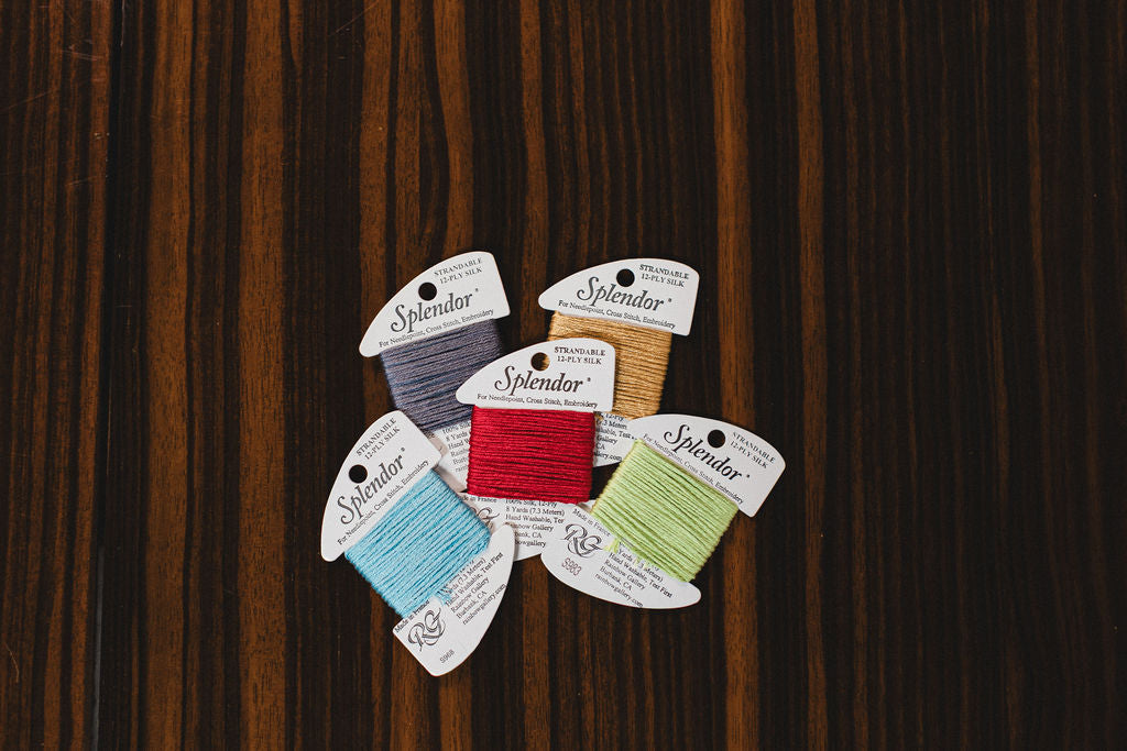 Collection of colorful thread spools with 'Splendor' labels on a wooden surface.  | The Pepper Pot Barrington, IL 