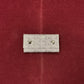 A small light gray monogram wallet with two silver snap buttons, displayed on a textured dark red background.