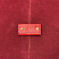 A small red leather pouch with two gold-tone metal rivets, centered on a textured red fabric background.